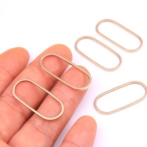May include: Five gold-coloured metal oval rings, some are held in a hand, others are on a white surface.