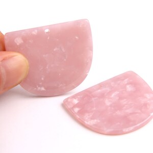 Puede incluir: Dos pendientes de resina de color rosa en forma de semicírculo con un patrón de mármol.