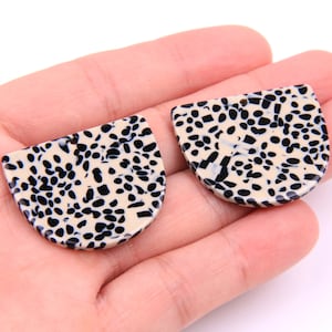 Könnte beinhalten: Zwei schwarze und weiße gemusterte halbkreisförmige Harzohrringe.