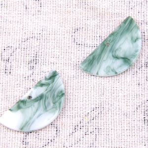 Puede incluir: Dos botones de plástico verde y blanco con forma de semicírculo y un agujero en el centro.