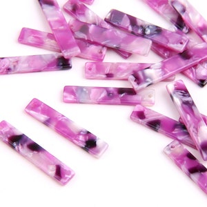 Puede incluir: Una colección de cuentas rectangulares de acrílico marmoleado en rosa y blanco con remolinos negros. Las cuentas tienen un agujero en cada extremo para enhebrar.