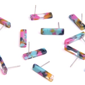 May include: Stud earrings with a rectangular shape and a marbled pattern in pink, blue, yellow, and black. The earrings have a post fitting for pierced ears. The earrings are displayed on a white surface.