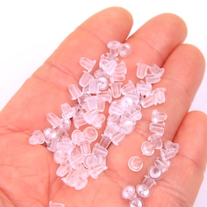 May include: A close-up of a hand holding a large quantity of clear plastic earring backs.