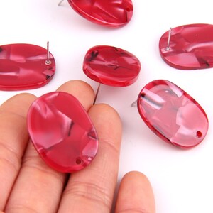 May include: Six red oval-shaped resin cabochons with a swirl pattern and a hole drilled through the top. The cabochons are approximately 1 inch in length and 1/2 inch in width.