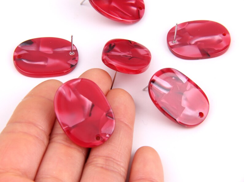 May include: Six red oval-shaped resin cabochons with a swirl pattern and a hole drilled through the top. The cabochons are approximately 1 inch in length and 1/2 inch in width.
