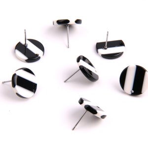 Puede incluir: Seis pares de pendientes redondos de botón a rayas blancas y negras. Los pendientes están hechos de un material blanco con rayas negras. Los pendientes están sobre un fondo blanco.