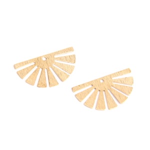 May include: Two gold-colored, half-circle shaped earring pendants. Each pendant has a sunburst design with a small hole at the top for attachment. The pendants are on a white background.