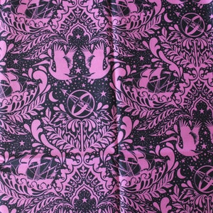 May include: Pink and black fabric with a repeating pattern of stylized ships, birds, and stars. The pattern is intricate and detailed, with a damask-like feel.