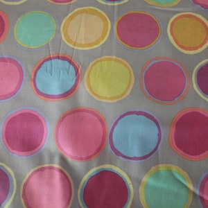 May include: A gray fabric with a repeating pattern of colorful circles. The circles are outlined in a darker shade of the same color and have a slightly faded appearance.