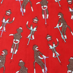 May include: Red fabric with a repeating pattern of brown sock monkeys riding scooters. The monkeys wear white gloves, socks, and hats. The scooters are light blue and purple.