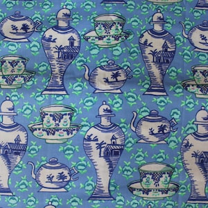 May include: Blue fabric with a repeating pattern of white and blue teapots, cups, saucers, and decorative vases. The design includes detailed illustrations of buildings and trees, set against a floral background.