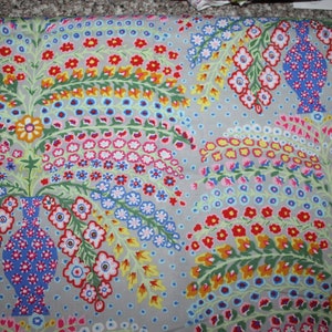 May include: A light gray fabric featuring a repeating pattern of blue vases filled with stylized flowers in red, yellow, pink, and green. The design includes arching floral branches and small blue dots scattered across the background surface.