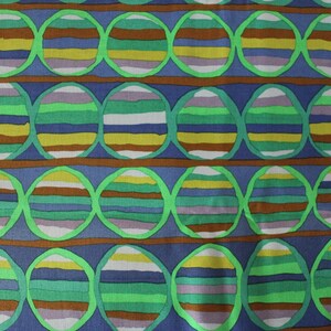 May include: A fabric with a repeating pattern of green, brown, blue, and yellow striped circles on a blue background.