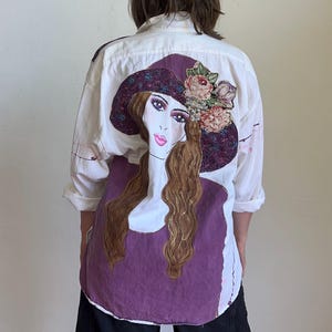 May include: A white ceramic mug with a black handle and the text "But First, Coffee" in a bold, black font. The mug is set against a blurred background, suggesting a cozy setting.