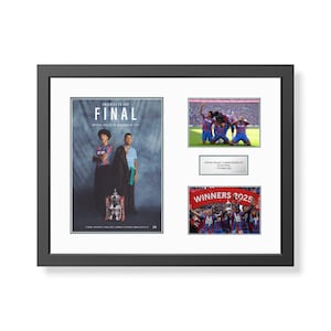 May include: Framed print with soccer-related imagery. It includes a poster with "FINAL", photos of players celebrating, a plaque, and a photo of the winning team with "WINNERS 2025". The frame is black and the print is mounted on white.
