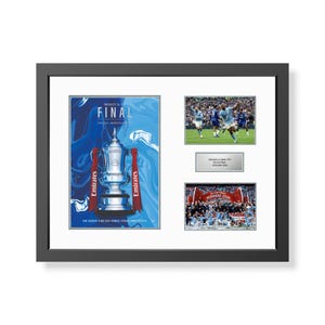 May include: Framed football memorabilia. The left side features a poster with a trophy and the word "FINAL". Two photos of the game and a winners banner are also included. The frame is black.