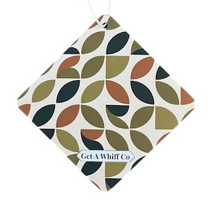 May include: A diamond-shaped air freshener with a geometric pattern of olive green, dark teal, and rust-colored shapes on an off-white background. The text "Get A Whiff Co" is printed on a small, rectangular label at the bottom.