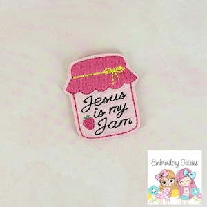 May include: A pink embroidered patch in the shape of a jam jar with the text "Jesus is my Jam" in black script. A small strawberry is next to the word "Jam". The jar has a pink lid with a yellow bow.
