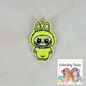 May include: Yellow felt applique of a monster wearing a bunny costume with black eyes and a toothy grin.