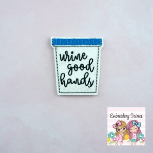 May include: White felt applique with blue trim shaped like a container with the text "wine good hands" in black embroidery.