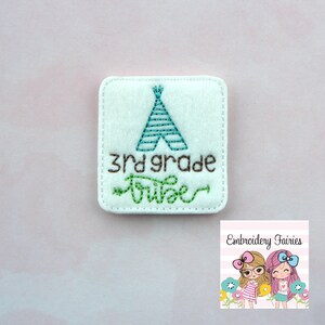 Puede incluir: Parche de fieltro blanco con bordado marrón que dice "3rd grade tribe" y un tipi bordado en verde y azul.