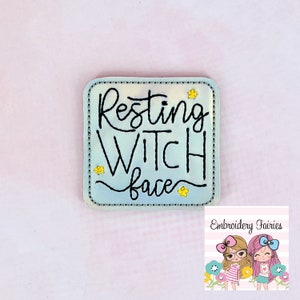 May include: A square, pale blue badge with the words "Resting Witch Face" in black script. The badge has a dotted border and small yellow star accents. The background is a soft pink.