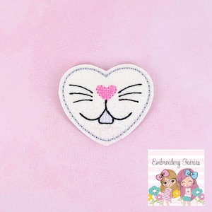 May include: A heart-shaped patch with a bunny face design. The patch features a white background with black whiskers and a pink heart-shaped nose. The edges are outlined with a dotted gray stitch. The image also includes the text "Embroidery Fairies".