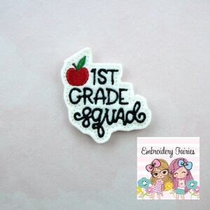 Puede incluir: Parche de fieltro blanco con bordado negro que dice "1st Grade Squad" con un gráfico de manzana roja.