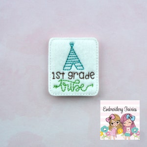 Puede incluir: Un parche cuadrado blanco con texto bordado y un diseño de tipi. El texto dice "1st grade tribe" en hilo marrón y verde. El tipi es turquesa. El parche es probablemente para una mochila o ropa.