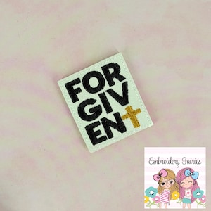 May include: A white embroidered patch with the words "FORGIVEN" in black block letters and a gold cross. The patch is rectangular with rounded corners. The background is a light pink.