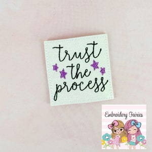 Può includere: Toppa quadrata in feltro bianco con ricamo nero che recita "trust the process" con stelle glitterate viola.