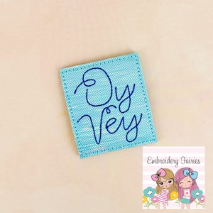 May include: A light blue square fabric patch with the words "Oy Vey" embroidered in dark blue thread.