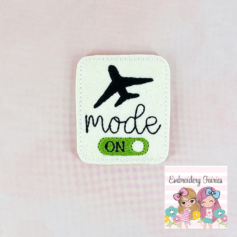 Pu&ograve; includere: Toppa in feltro bianco con ricamo nero di un aereo e le parole "mode on". L'interruttore &egrave; verde.