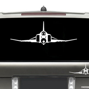 May include: White vinyl decal of a jet fighter plane, applied to the rear window of a gray SUV. The decal is a detailed silhouette of the aircraft. A smaller version of the decal is on the lower tailgate.