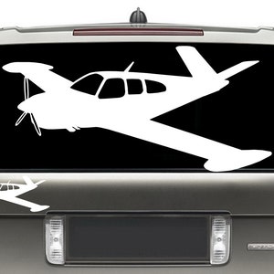 Puede incluir: Una silueta blanca de un avi&oacute;n peque&ntilde;o sobre un fondo negro. El avi&oacute;n se muestra de perfil con las alas extendidas. El avi&oacute;n est&aacute; en la ventana trasera de un SUV plateado.