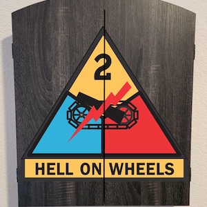 May include: A dark gray wood-grain dartboard cabinet with two doors. The front features the 2nd Armored Division insignia, a triangle divided into yellow, blue, and red sections with a black tank track, a red lightning bolt, the number 2, and the text HELL ON WHEELS.
