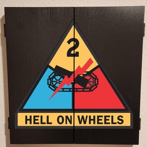 May include: A black wooden cabinet with two doors featuring a large triangular emblem of the 2nd Armored Division. The emblem displays a yellow top section with the number 2, a blue left section, a red right section, a black tank track, a red lightning bolt, and a yellow banner at the bottom with the text HELL ON WHEELS.