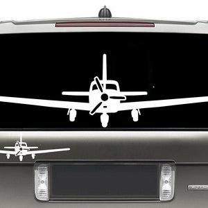 May include: A white silhouette of a small airplane with a propeller on the back is displayed on the back window of a silver SUV.