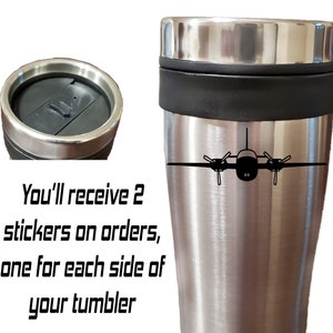 以下が含まれることがあります： 黒い蓋と中央に黒いバンドが付いたステンレス製のトラベルマグ。マグには、前面に小さな飛行機の黒いシルエットが描かれています。マグの下には、「You'll receive 2 stickers on orders, one for each side of your tumbler」というテキストが印刷されています。
