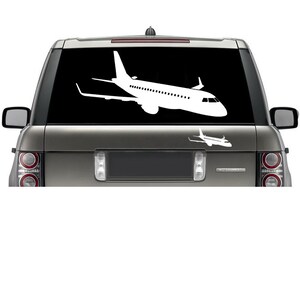 May include: A white silhouette of a plane is on the back window of a silver SUV. The plane is facing to the right and has a smaller plane silhouette below it.