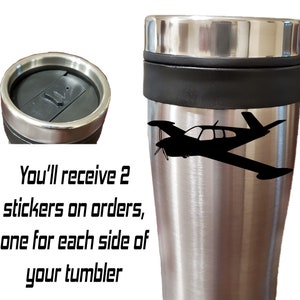 Puede incluir: Taza de viaje de acero inoxidable con una silueta de avi&oacute;n negra en el lateral. La taza tiene una tapa negra y una banda negra alrededor del medio. "You'll receive 2 stickers on orders, one for each side of your tumbler" est&aacute; escrito en negro debajo de la taza.