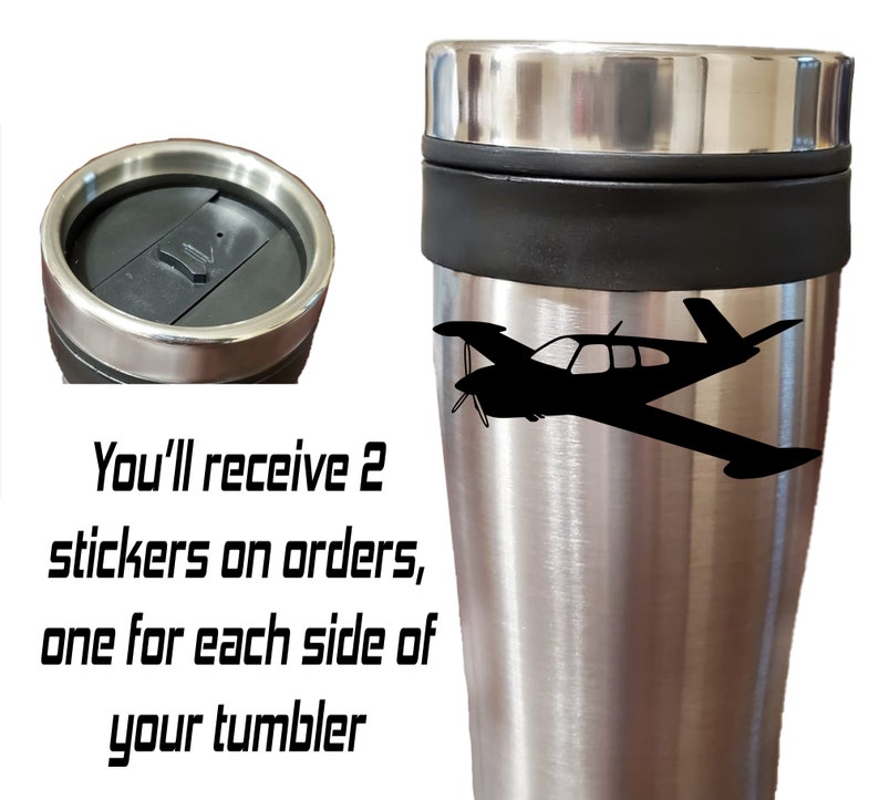 Puede incluir: Taza de viaje de acero inoxidable con una silueta de avi&oacute;n negra en el lateral. La taza tiene una tapa negra y una banda negra alrededor del medio. "You'll receive 2 stickers on orders, one for each side of your tumbler" est&aacute; escrito en negro debajo de la taza.
