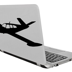 Puede incluir: Un ordenador port&aacute;til plateado con una silueta negra de un avi&oacute;n peque&ntilde;o en la tapa.