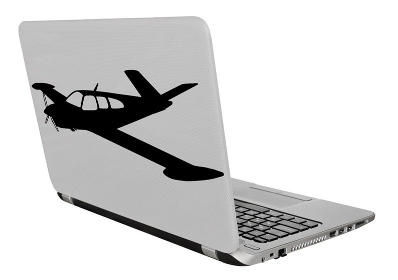 Puede incluir: Un ordenador port&aacute;til plateado con una silueta negra de un avi&oacute;n peque&ntilde;o en la tapa.