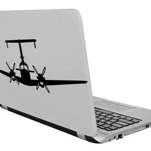 以下が含まれることがあります： 背面に双発プロペラ機の黒いシルエットが描かれた銀色のラップトップ