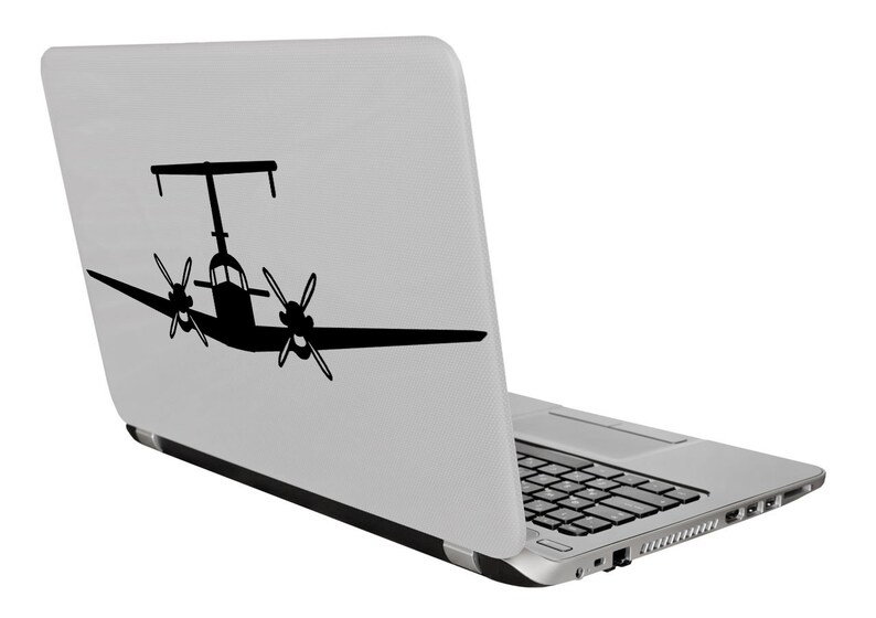 以下が含まれることがあります： 背面に双発プロペラ機の黒いシルエットが描かれた銀色のラップトップ