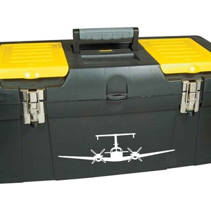 以下が含まれることがあります： 黄色いふたが付いた黒い工具箱で、白い飛行機のステッカーが貼られています。工具箱は両側に2つのラッチと上部にハンドルが付いています。
