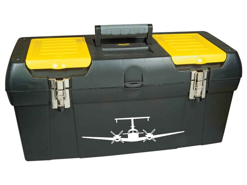 以下が含まれることがあります： 黄色いふたが付いた黒い工具箱で、白い飛行機のステッカーが貼られています。工具箱は両側に2つのラッチと上部にハンドルが付いています。