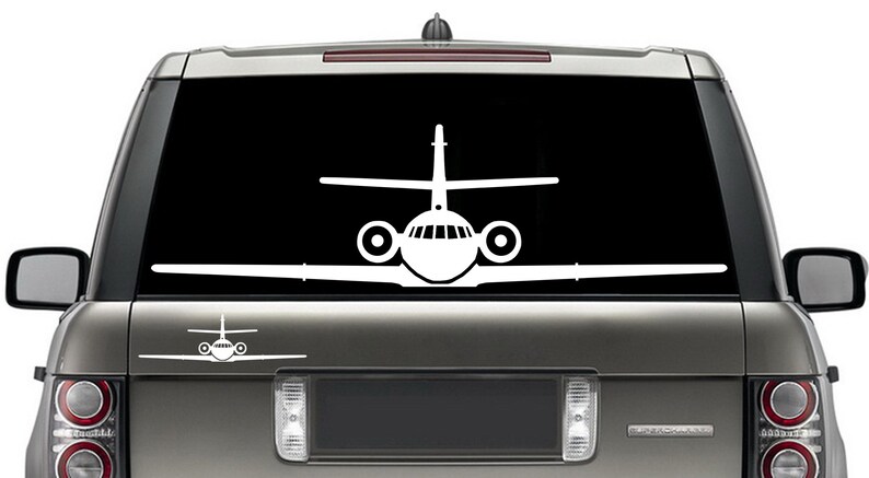 May include: A white silhouette of a private jet is displayed on the back window of a silver SUV. The jet is facing forward with the wings spread out.