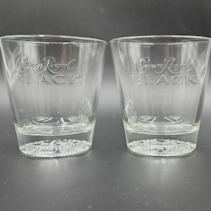 Może przedstawiać: Dwa przezroczyste szklanki typu lowball z wytłoczonym napisem "Crown Royal BLACK". Szklanki mają grubą podstawę z teksturowanym, wzorzystym wzorem. Szklanki są przeznaczone do serwowania whisky lub innych alkoholi.